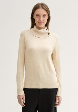 Pull col roulé beige avec un col à côtes, doté de deux boutons noirs sur le côté gauche, fabriqué en tissu doux et texturé.