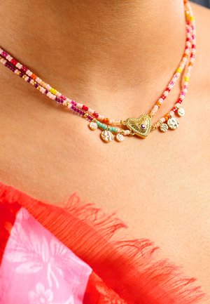Collier à plusieurs rangs de perles colorées en rose, orange et bleu sarcelle, avec un pendentif en forme de cœur doré et de petits charms décoratifs.