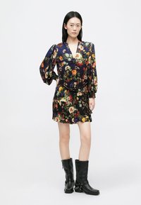 Rövid virágmintás ruha sötét, mintás anyagból, élénk virágokkal. Puffos ujjakkal, mély dekoltázzsal, és fekete, térd fölé érő csizmákkal párosítva.