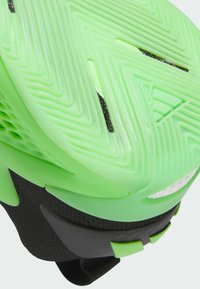 Grøn gummisål med zigzag-mønster, tekstureret sort sidepanel og integreret hælkop. Har små sorte detaljer.