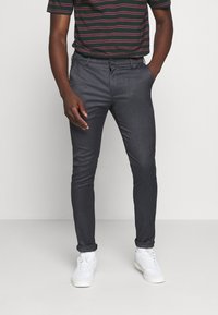 Pantalon gris foncé ajusté en tissu texturé. Il présente un devant plat, des passants de ceinture et des détails de poche subtils. Portez-le avec des baskets blanches.
