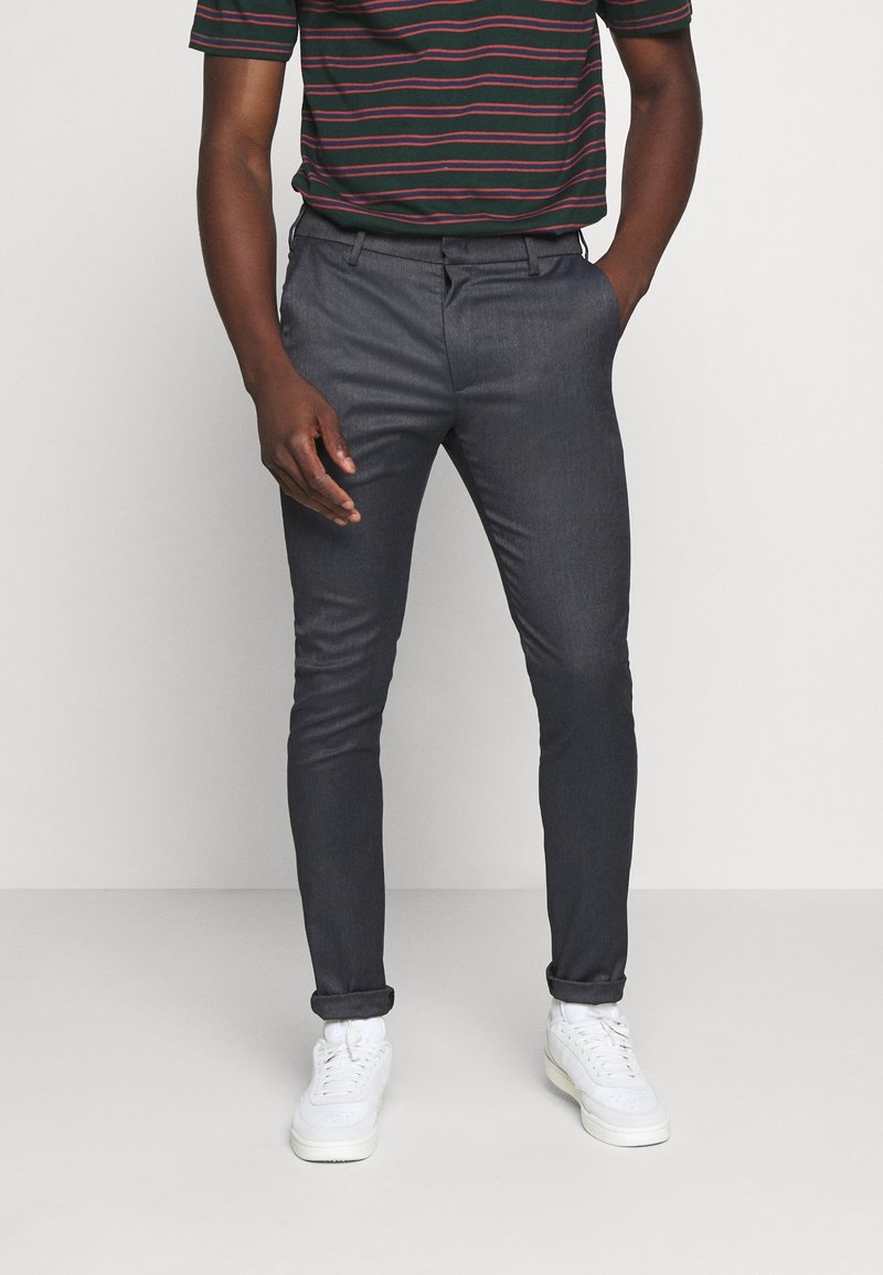 Pantalon gris foncé ajusté en tissu texturé. Il présente un devant plat, des passants de ceinture et des détails de poche subtils. Portez-le avec des baskets blanches.