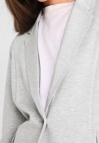 Grå blazer i blandning av bomull, med slagkrage, enkelknäppning och slät yta, lager på lager över en ljusrosa topp.