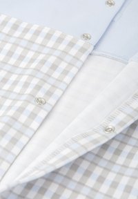 Camisa de algodón azul claro con un patrón de cuadros en gris y blanco. Presenta botones a presión y una textura suave, con un cuello y tejido interior de contraste.