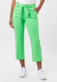 Groene, op maat gemaakte pantalon met een strikceintuur, cropped lengte, gladde textuur, aansluitende taille en zijzakken, gecombineerd met witte sneakers.