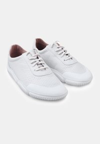 White athletic shoes feature perforated leather, lace closure, and rubber sole with textured accents. Soft interior lining enhances comfort.