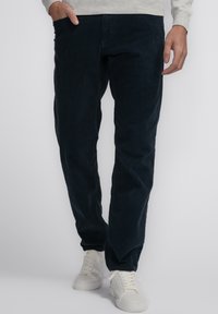Marineblauwe corduroy broek met een rechte snit en subtiele ribbelstructuur, gedragen met witte sneakers. Heeft zijzakken voor functionaliteit.