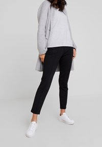 Rento asu, joka koostuu vaaleanharmaasta, teksturoidusta neuleesta, mustista slim fit -housuista ja valkoisista lenkkareista. Yksinkertainen muotoilu ja neutraalit värit.