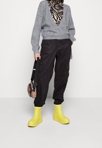 Grå stickad tröja, svarta cargo-byxor, gula gummistövlar och en liten väska i leopardmönster. Märkbara texturer och kontrasterande färger.