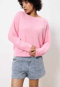 Helles rosa, strukturiertes Strickoberteil mit lockerem Schnitt und weitem Ausschnitt, kombiniert mit hellblauen Denim-Shorts mit Fronttaschen.