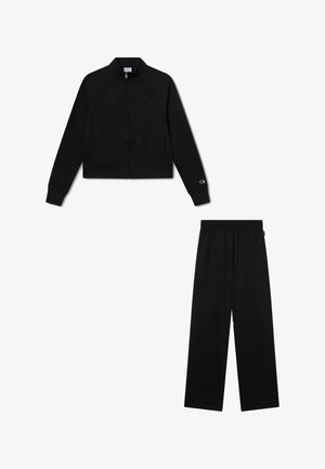 Schwarze Reißverschlussjacke mit langen Ärmeln und schwarze, weit geschnittene Hose, beide mit dezenten Logodetails an Ärmeln und Taille.