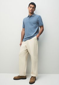 Ljusblå pikétröja med kontrasterande randig krage, kombinerad med lösa beiga byxor och bruna mockaskor. Enkel design och avslappnad passform.