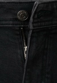 Schwarze Jeans aus Denim zeigen einen Metallknopf und einen Reißverschluss. Der Stoff weist eine subtile Textur und sichtbare Nähte entlang der Nähte auf.