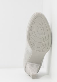 Sko med en texturerad ljusgrå mockaovandel, med en mönstrad gummisula och en klack med ett randigt mönster.