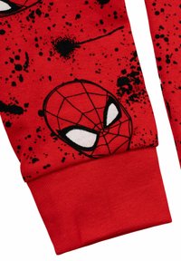 Manica in tessuto rosso con macchie di vernice nera e una grafica di una maschera di Spider-Man in bianco e nero vicino al polsino.