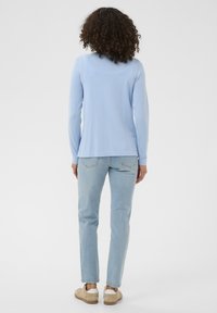 Hellblaues Langarmshirt mit rundem Ausschnitt, kombiniert mit hellblauen Jeans mit geradem Bein und beigen Schuhen. Weicher Stoff und schlichtes Design.