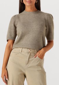 Licht olijfgroen gebreid truitje met korte pofmouwen. Ronde halslijn en zachte textuur. Gecombineerd met beige high-waisted jeans.