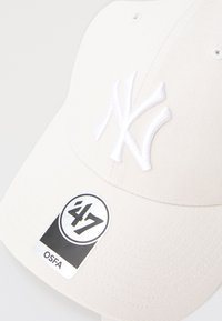 Cappellino da baseball bianco realizzato in tessuto testurizzato con un logo "NY" ricamato, completo di un'etichetta bianca e nera che recita "47 OSFA."