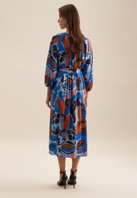 Langes, blaues Kleid mit einem floralen Muster in Rot, Braun und Marineblau. Hergestellt aus leichtem Stoff mit einem taillierten Bereich und puffigen Ärmeln.
