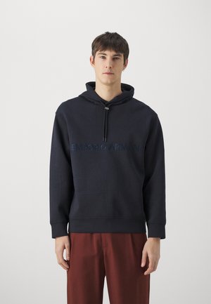 Sudadera con capucha de color azul marino con costuras texturizadas y el logo de "Emporio Armani" destacado en el pecho. Material de mezcla de algodón.