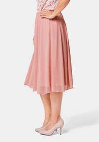 Lichtroze midi rok van vloeiende stof, met een geplooid ontwerp en een elastische tailleband. Gecombineerd met bijpassende blush hoge hakken.