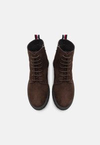 Botas de tobillo de ante marrón con un cierre de cordones en la parte delantera y cremallera. Suela de goma con un acabado texturizado. Asas de acento en rojo, blanco y azul.