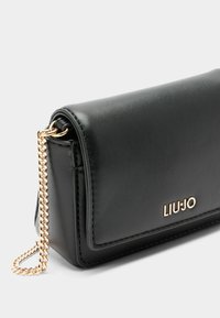 Portafoglio in ecopelle nera con una tracolla in catena dorata, caratterizzato da una texture liscia e un logo impresso sul davanti. Design rettangolare compatto.