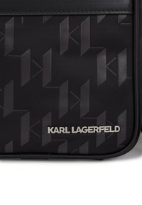 Borsa nera con texture, caratterizzata da un motivo geometrico ripetuto, dettagli del logo in argento e un design elegante con bordi lisci.