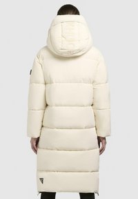 Long cream puffer coat with a high collar and oversized hood, featuring horizontal quilted sections and a brand logo on the hood.