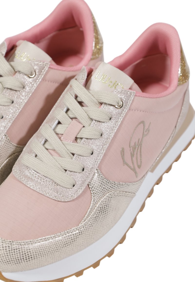 Zapatillas rosa claro con acentos metálicos, paneles texturizados y suelas blancas. Presenta cordones beige y un logotipo en relieve en el lateral.