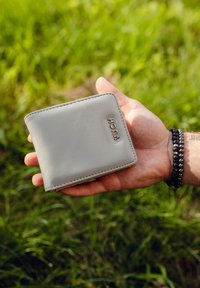 Gray leather wallet with rounded corners, featuring embossed brand name. The surface is smooth with subtle stitching details.