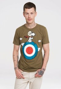 Olivenfarbiges Baumwoll-T-Shirt mit einem Cartoon-Hund, der eine Brille und einen Schal trägt, sitzt auf einem blauen und roten Ziel-Design, umgeben von weißen Wolken.