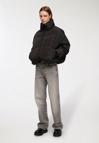 Giubbotto a piuma nero con colletto alto, vestibilità oversize e design trapuntato; abbinato a jeans grigi a gamba dritta e stivali neri con plateau.