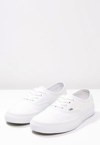 White canvas sneakers with a low-top design, round toe, and lace-up closure. Features rubber outsole and stitched detailing.