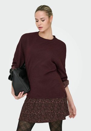 Maglione bordeaux con una vestibilità morbida, caratterizzato da maniche arrotolate. Abbinato a una mini gonna a fantasia in tonalità scure e collant a rete. Borsa nera.