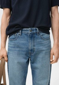 Lichtblauwe denim jeans met een klassieke pasvorm, voorzien van een knoopsluiting, voortassen en contrasterende stiksels, gecombineerd met een donker shirt.