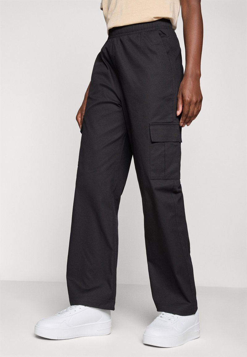 Pantaloni cargo neri realizzati in tessuto leggero, con vita elastica e tasche laterali, abbinati a sneaker bianche.