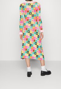 Robe en tricot à manches longues, présentant des carrés et motifs multicolores, principalement en rose, vert et jaune. Accentuée par des poignets roses.