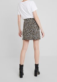 Leopardmönstrad minikjol med en åtsittande design, texturerat tyg och dragkedja bak. Bärs med en enkel vit t-shirt och svarta ankelstövlar.