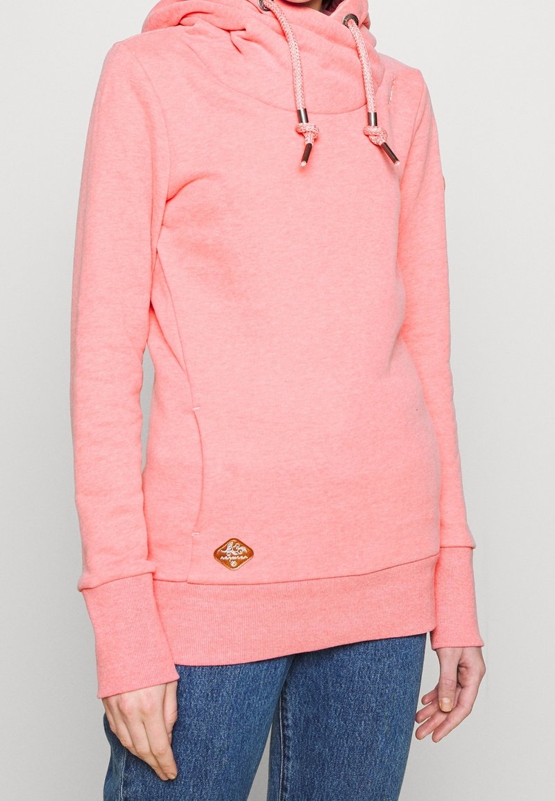 Korall hoodie med hög hals, dragsnören och en texturerad yta. Har en liten brun logotyp på sidan och ribbade ärmslut.