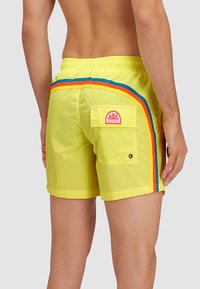 Costumi da bagno gialli con finitura testurizzata, caratterizzati da strisce multicolor orizzontali sui lati e una tasca sul retro con un'etichetta del logo.