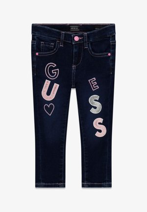 Dunkelblaue Kinderjeans mit pinken und silbernen Glitzerbuchstaben, die "GUESS" buchstabieren, und einem kleinen Herz auf den Vorderbeinen.