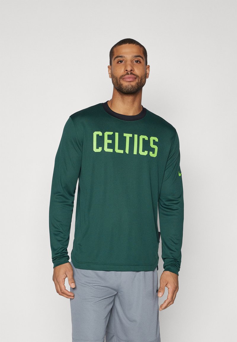 Žalia ilgomis rankovėmis sportinė marškinė, kuriose išryškintos ryškiai geltonai žaliai užrašytos "CELTICS" raidės per krūtinę, su apvalia iškirpte ir tekstūruotu audiniu.