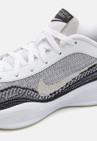 Białe buty sportowe z siateczkową cholewką w szarym i czarnym wzorze, z teksturowanym logo Nike oraz płaskimi białymi sznurowadłami, oznaczone "GT HUSTLE".
