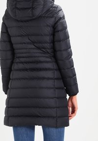 Black puffer coat with a hood, featuring horizontal quilted lines and a slightly tapered waist, made from shiny, smooth material.