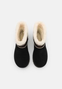 Botas negras hasta el tobillo con un suave forro y ribete de pelo sintético blanco, que presentan costuras decorativas alrededor del tobillo. Punta redonda y suela plana.