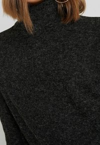 Suéter negro de cuello alto fabricado en punto texturizado, que presenta un alto cuello y un acabado suave y borroso, con un corte holgado.