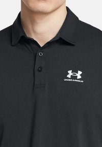 Polo shirt nera con colletto strutturato, placca con due bottoni e logo Under Armour bianco ricamato sul lato sinistro del petto.