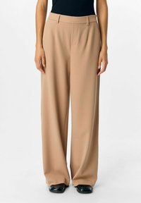 Beige breddebenede bukser i glat stof, med en skræddersyet pasform, sidelommer og et høj talje-design. Sorte sko fuldender looket.
