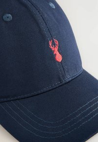 Gorra azul marino de algodón con el logo de langosta roja bordado, costuras en contraste y seis agujeros de ventilación con acentos azules.